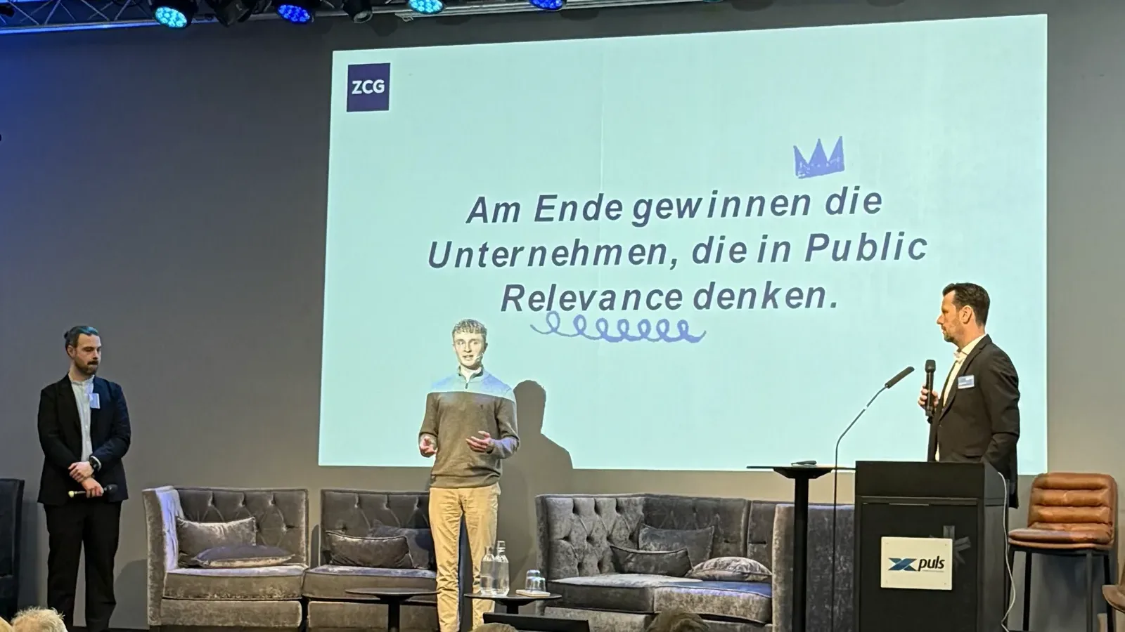 Charles Bahr auf der Bühne vor einer Folie mit dem Satz, dass am Ende die Unternehmen gewinnen, die in Public Relevance denken